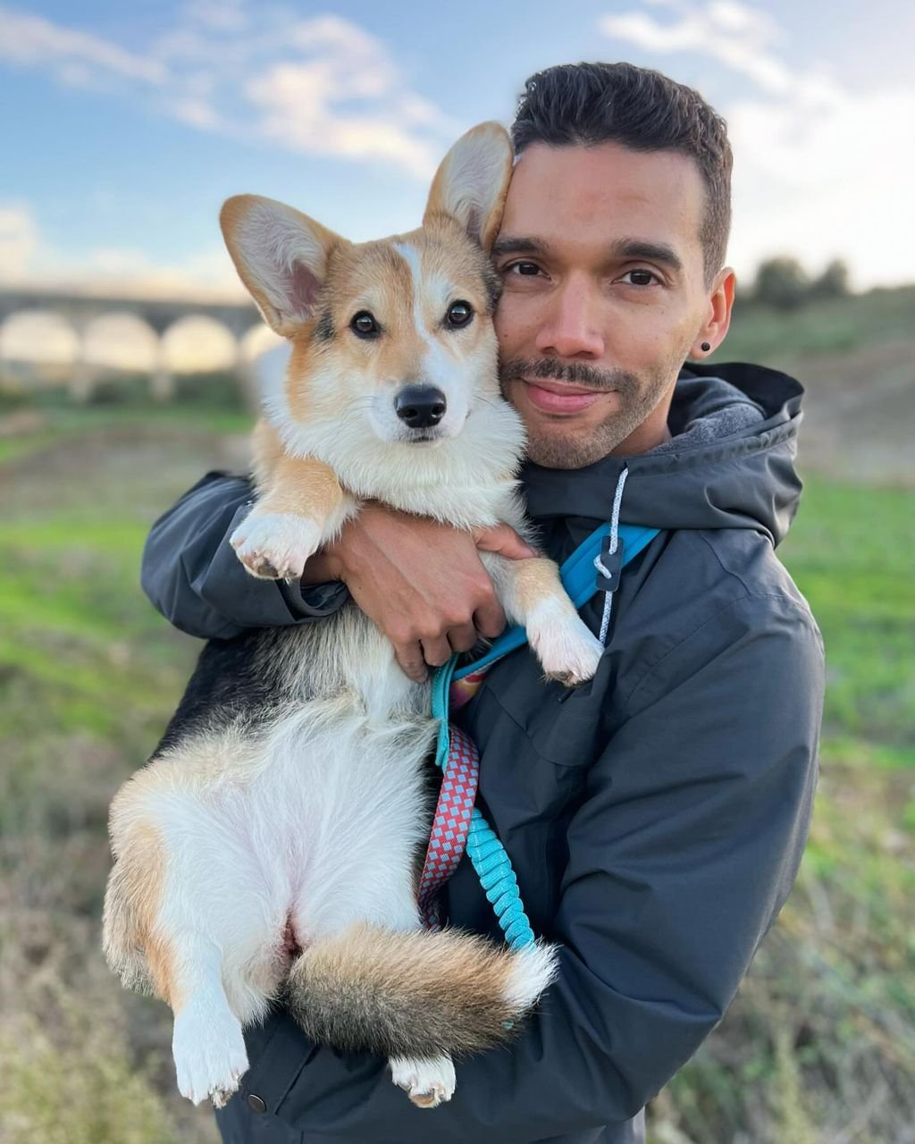 Man outdoors holding tri-color Corgi with blue sky