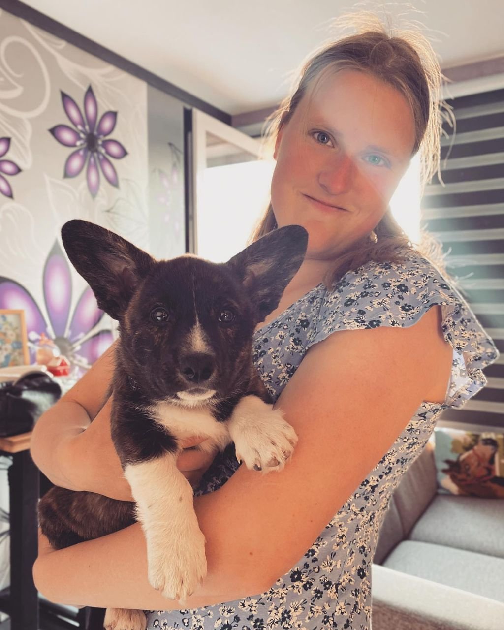 Woman holding black and white Corgi puppy in a floral room