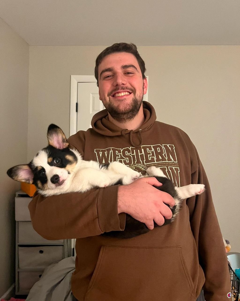 Young man cuddling black and tan Corgi indoors